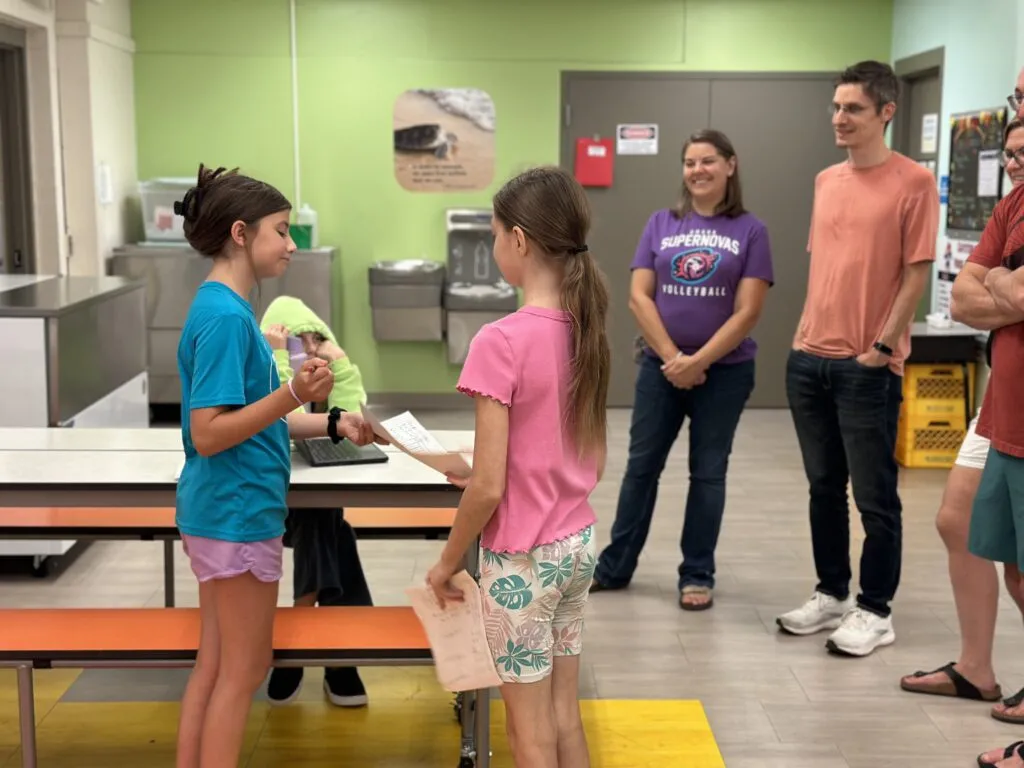 A small group of adults listens to two students present a class project.
