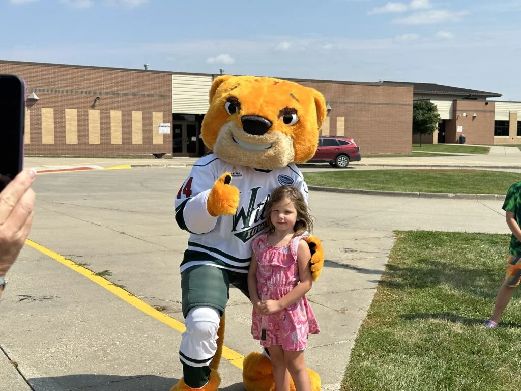 Elementary student poses for a picture with the Iowa Wild hockey team wildcat mascot. The mascot gives a thumbs up.