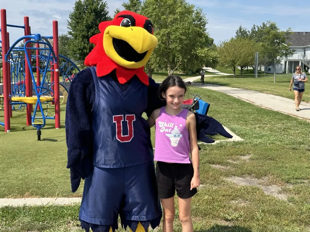 Elementary student stands and smiles with the J-Hawk mascot.