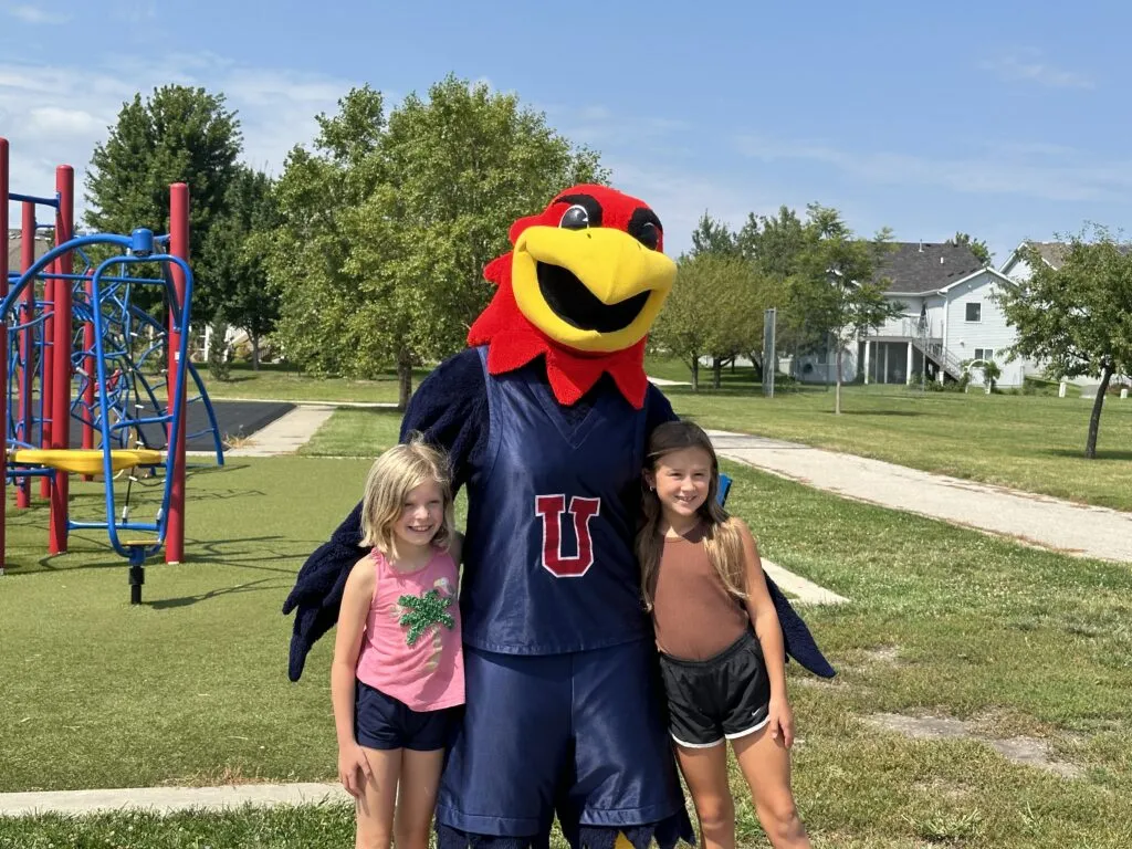 Two elementary students stand and smile for a picture with the J-Hawk mascot.