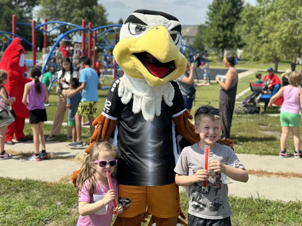 Two elementary students holding red popsicles stand and smile with an eagle mascot.