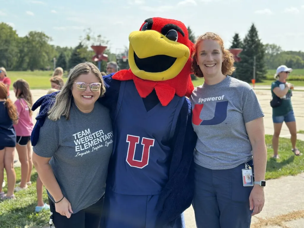 Two teachers stand and smile with the J-Hawk mascot
