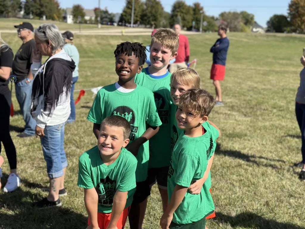 Five elementary students in green shirts smile for the camera.